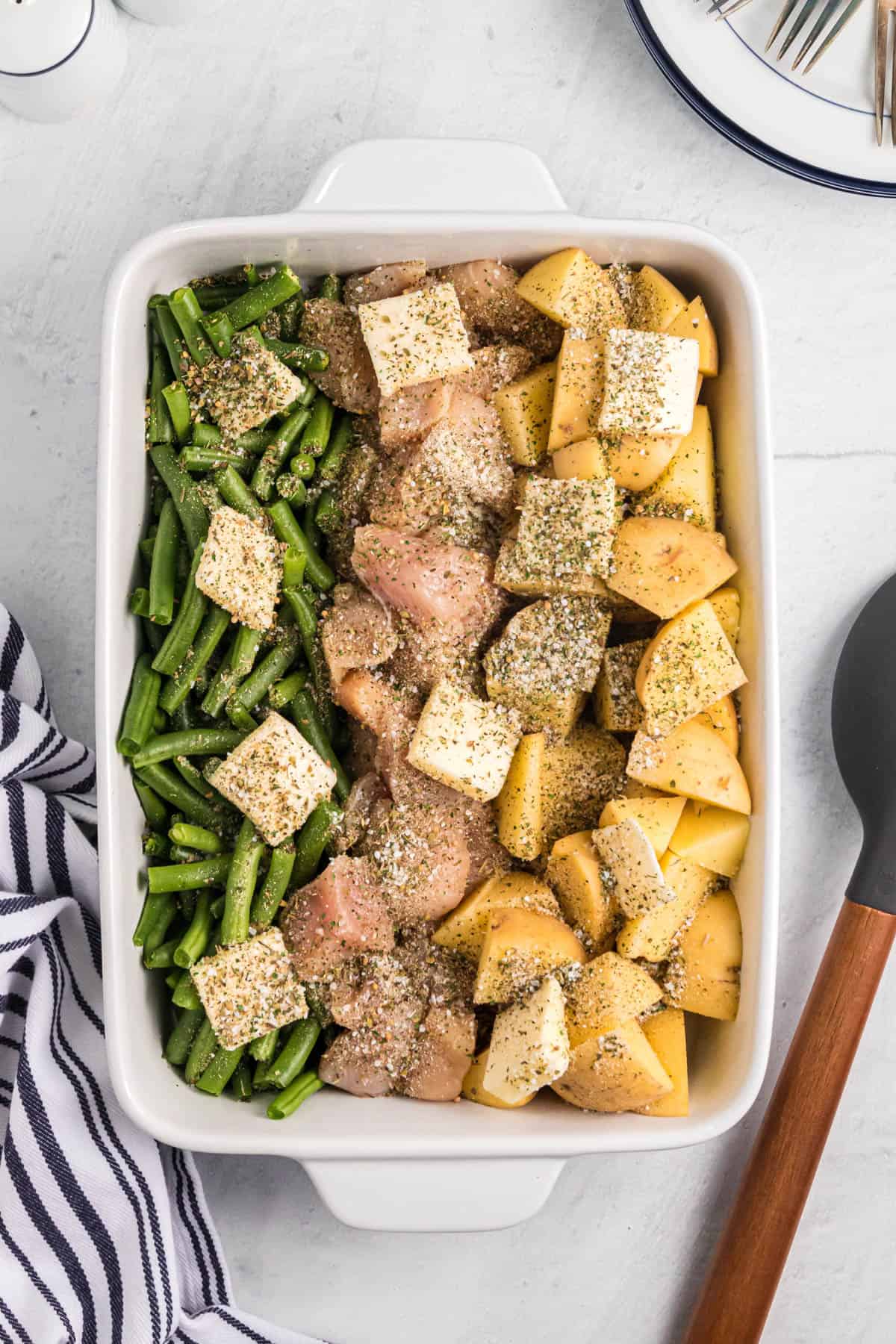 Herbs and seasoning sprinkled on top of vegetables, chicken, and potatoes in a pan.