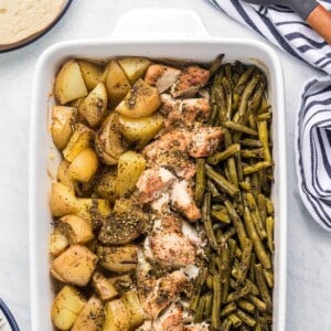 A large white baking dish with rows of potato chunks, chicken pieces, and green beans.