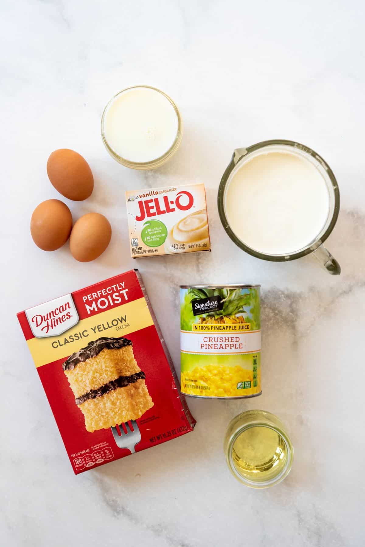 Ingredients for making a pineapple poke cake on a white surface.