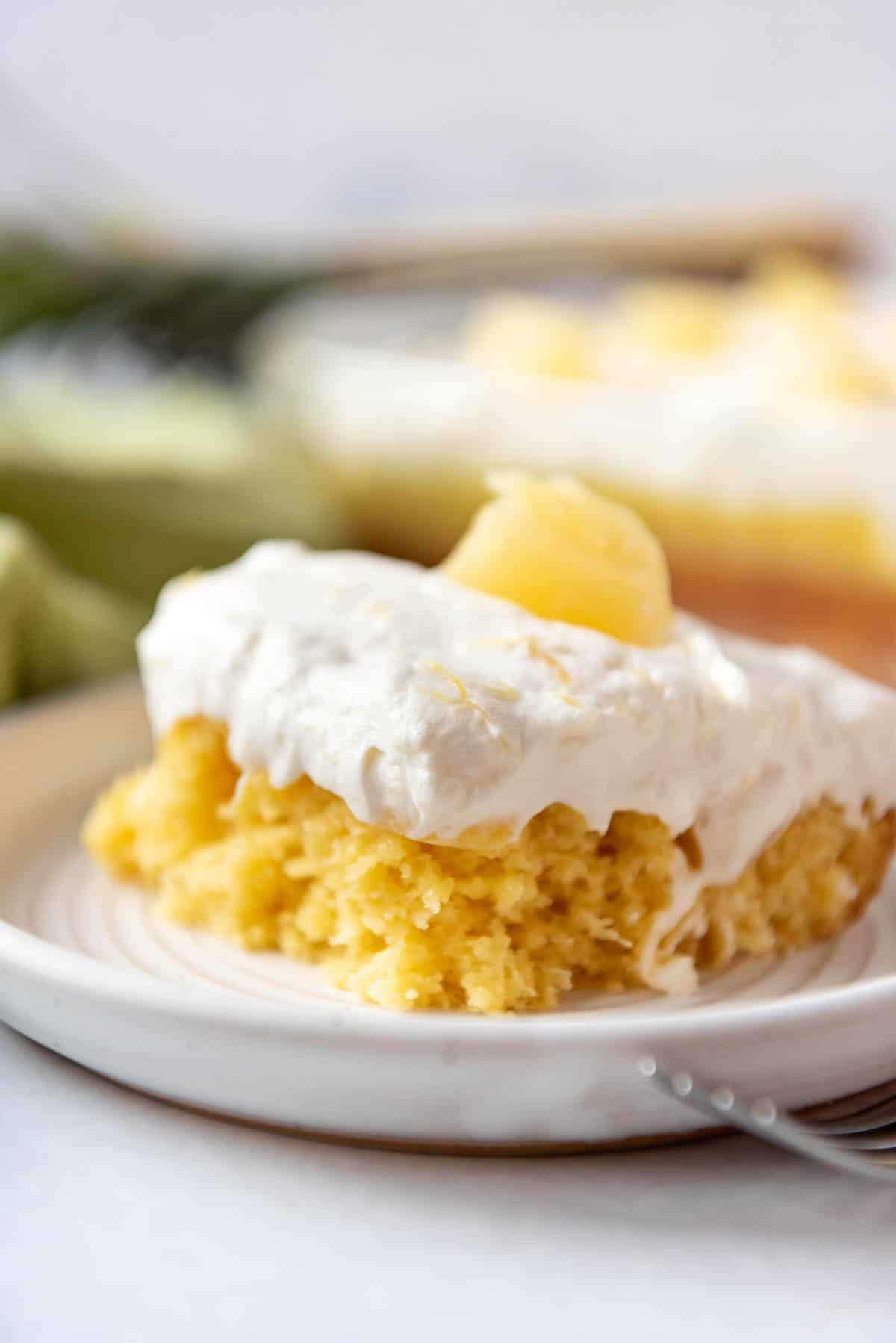 A side image of a slice of pineapple poke cake on a white plate.