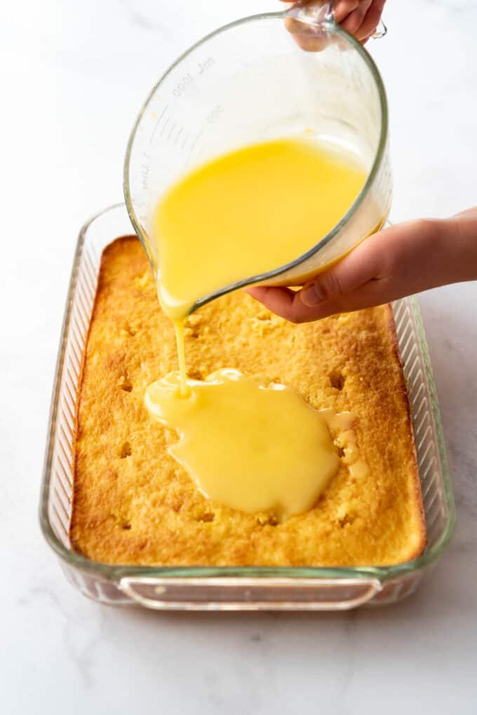 Pouring pudding over a yellow poke cake made with crushed pineapple.