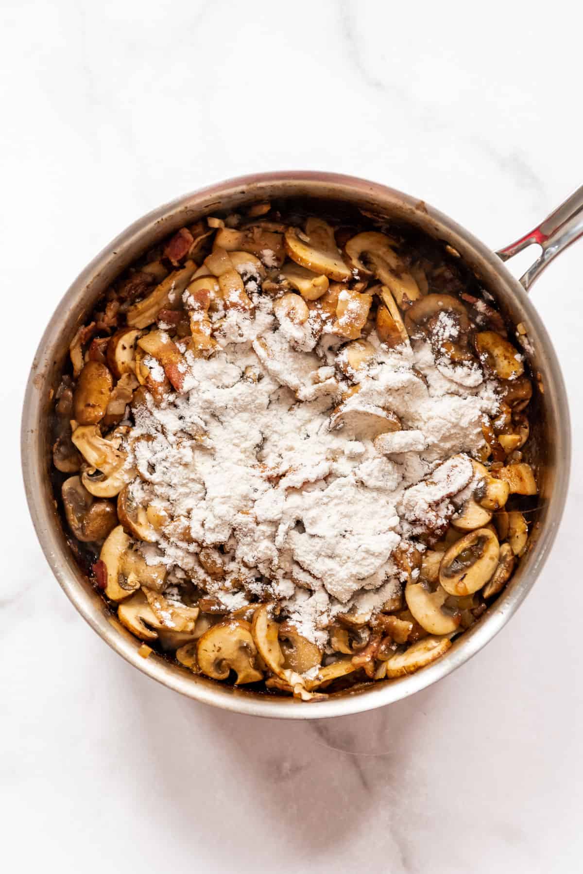 Flour sprinkled over sauteed mushrooms and onions in a pan.