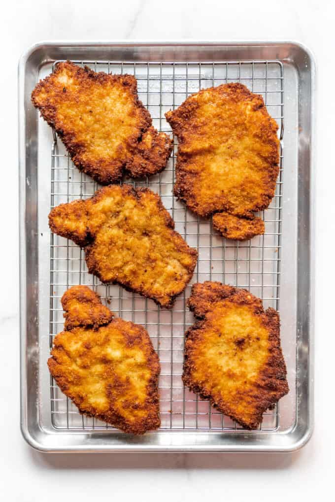 Crispy fried pork schnitzel on a baking sheet lined with a wire rack.