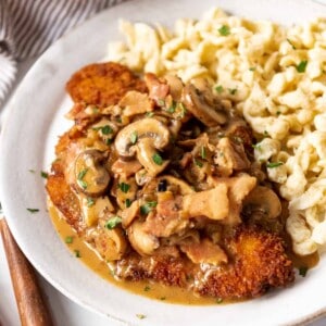 Jagerschnitzel with mushroom sauce and spaetzel on a white plate.