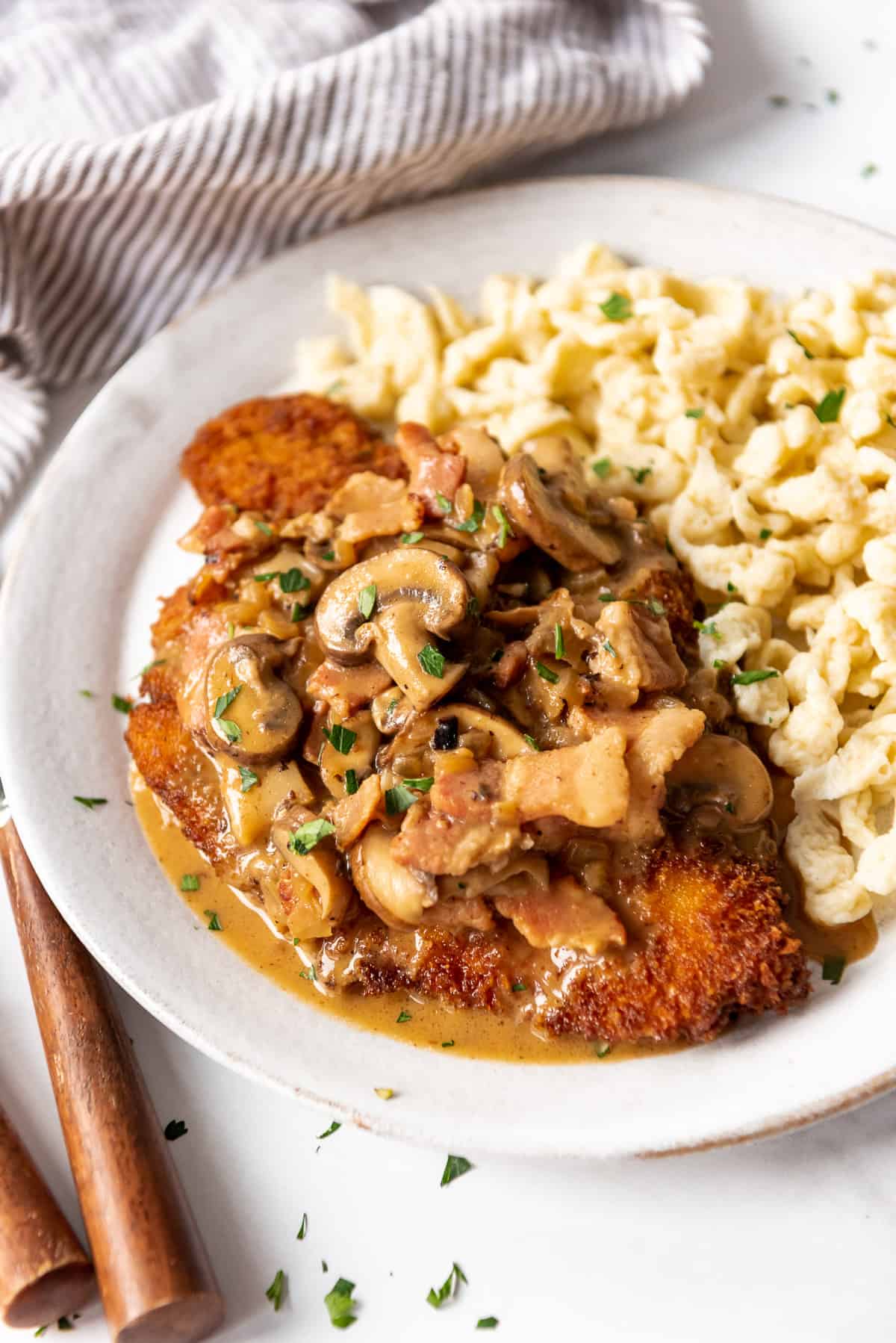 Jagerschnitzel with mushroom sauce and spaetzel on a white plate.