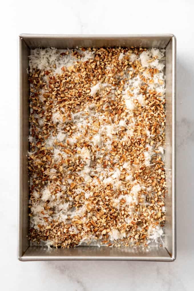 Shredded coconut and chopped pecans sprinkled over the bottom of a rectangular baking dish.