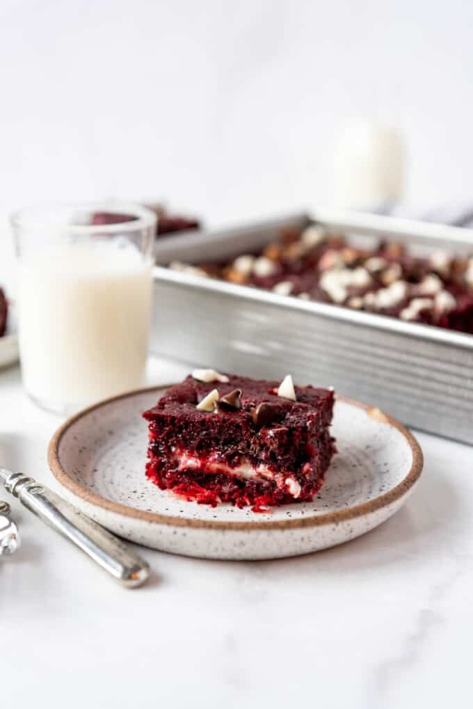 A piece of red velvet earthquake cake with cream cheese swirl on a plate in front of the rest of the cake.