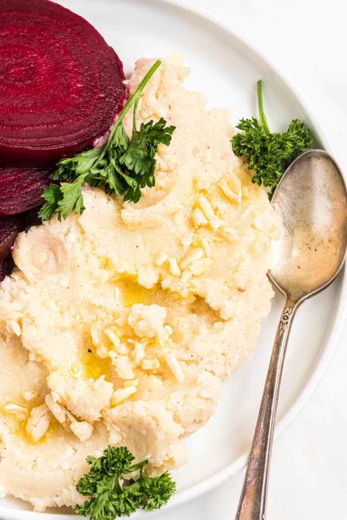 A pile of Greek skordalia garlic potato spread on a white plate with roasted red beets and a spoon.