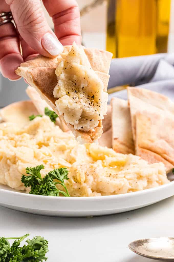A hand holding a pita triangle topped with Greek skordalia garlic potato spread.