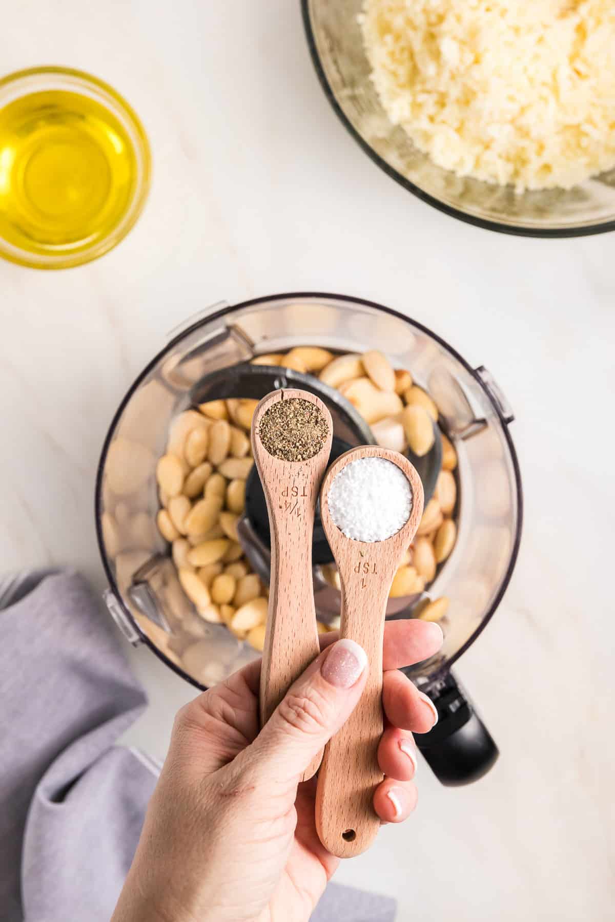 Adding salt and pepper to garlic and almonds in a food processor.