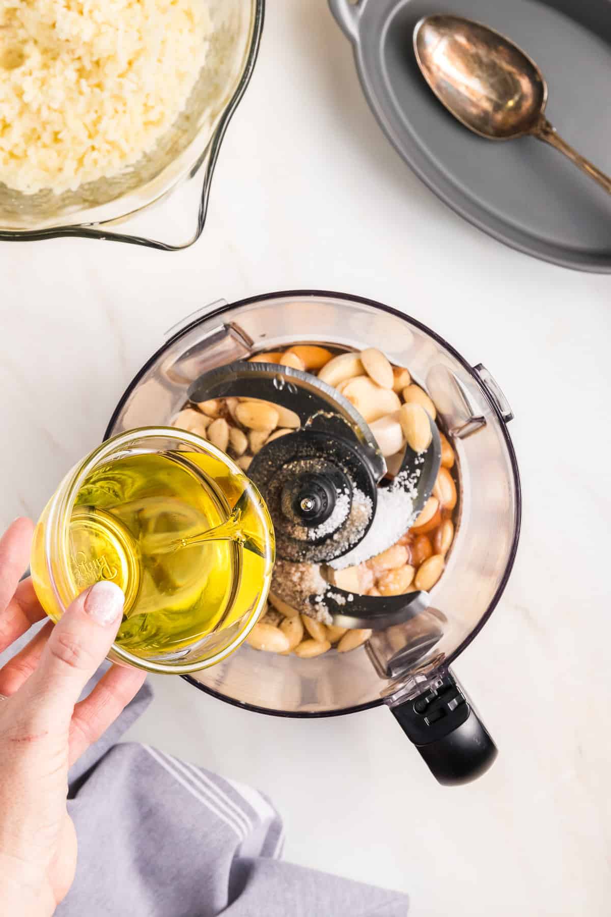 Adding olive oil to almonds and garlic in a food processor.