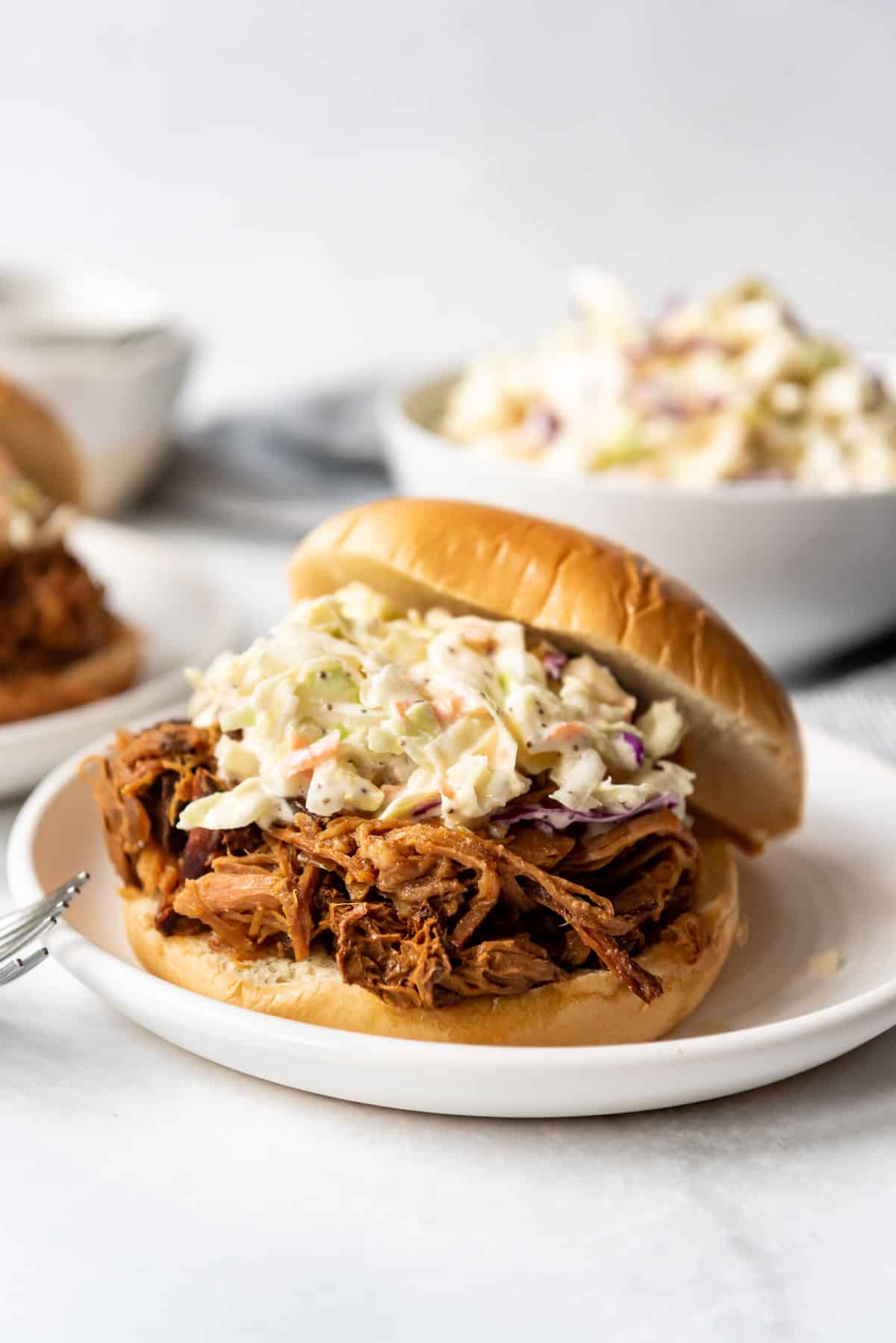 An apricot pulled pork sandwich topped with homemade coleslaw on a white plate.