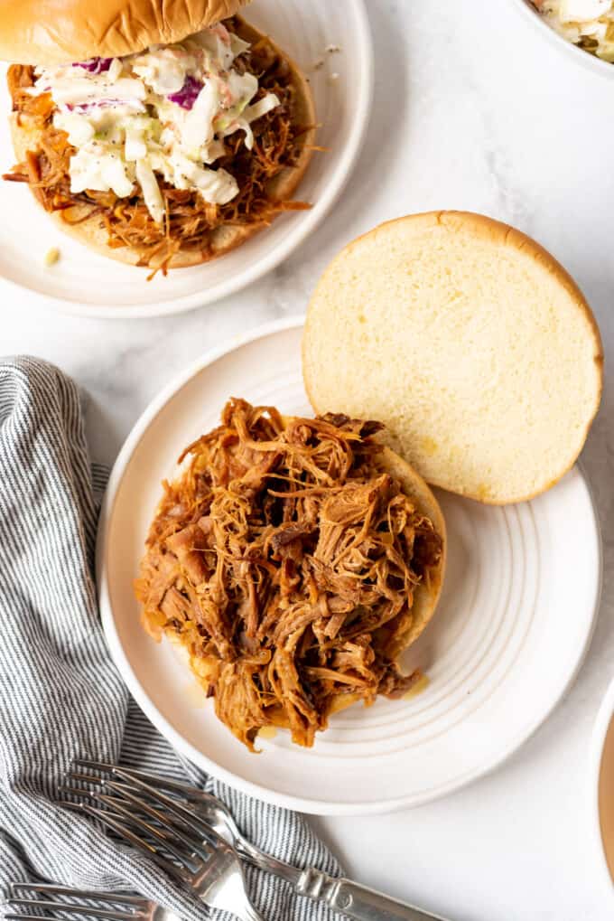A bun topped with pulled pork on a white plate.
