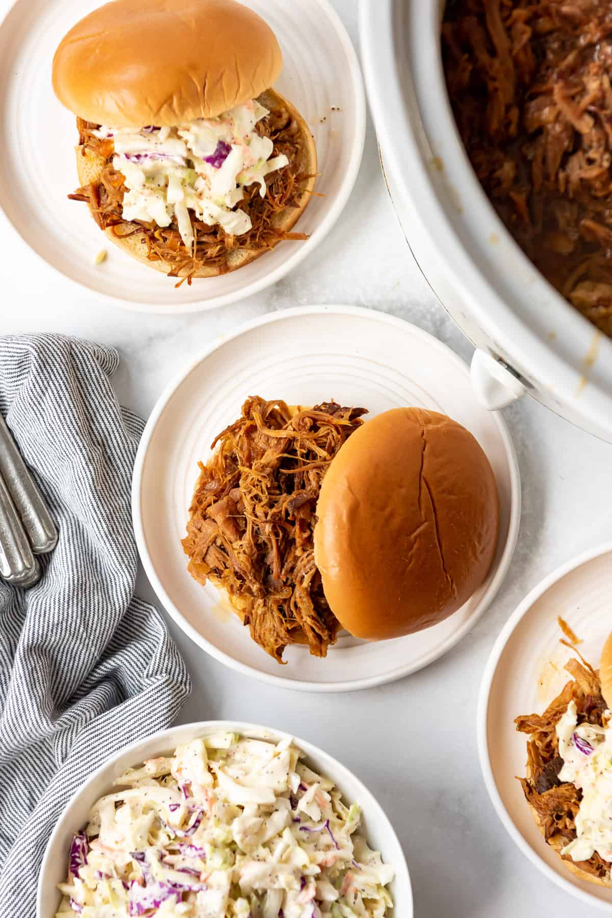 An overhead image of a buns topping pulled pork sandwiches on white plates.