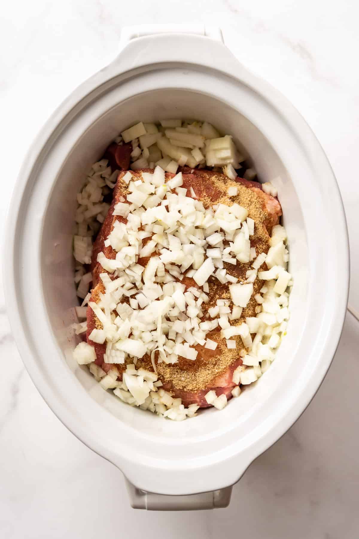 Adding chopped onions to a pork roast in a slow cooker.