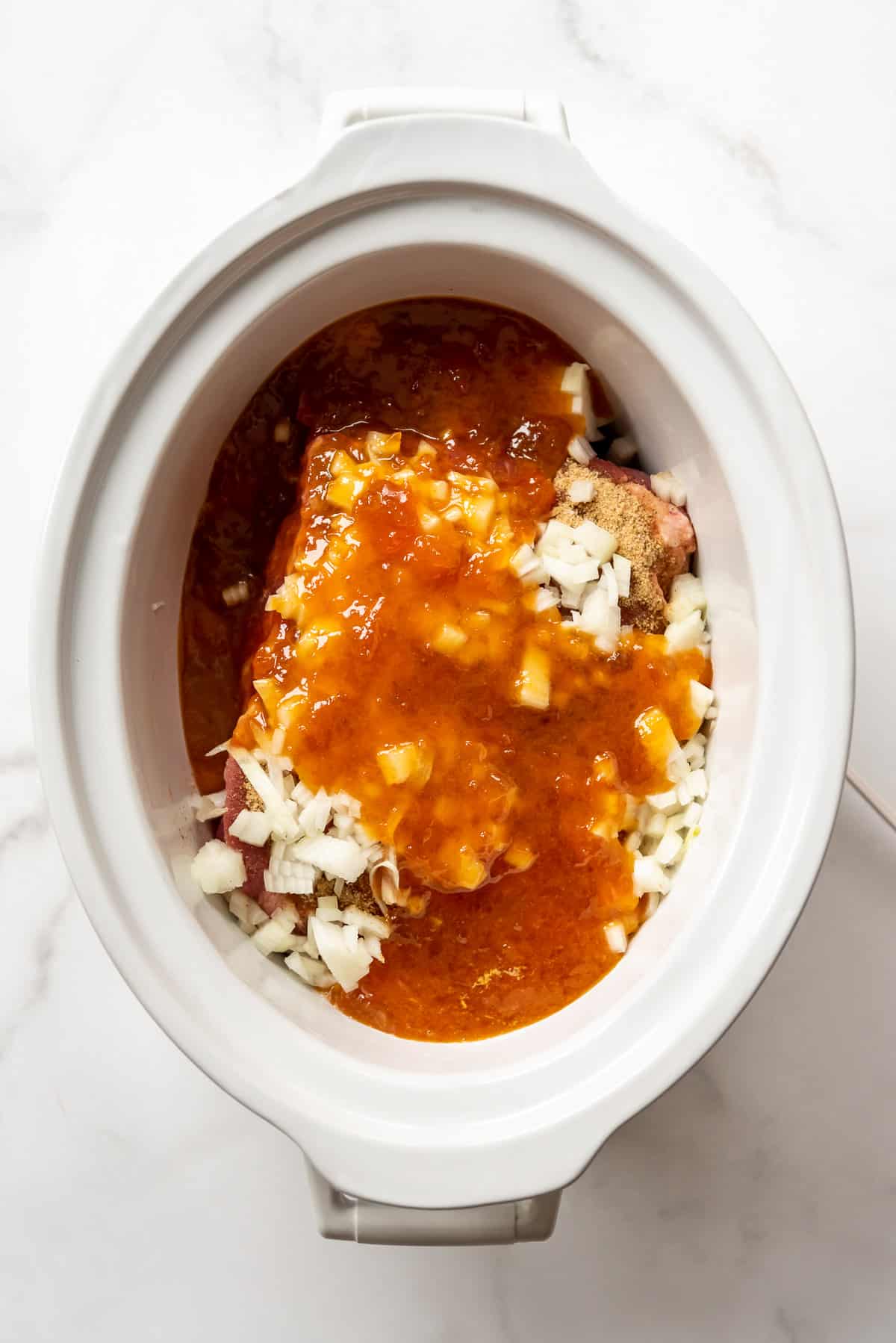 Apricot preserves poured over onions and a pork roast in a white crockpot.