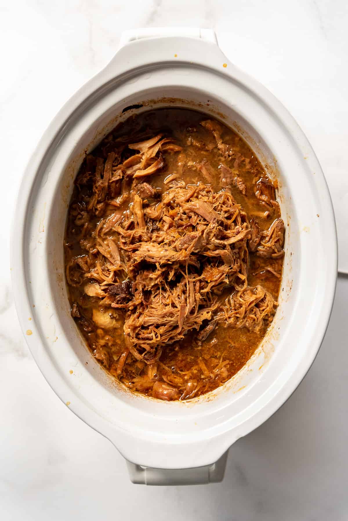 A white crockpot with pulled pork in an apricot sauce.