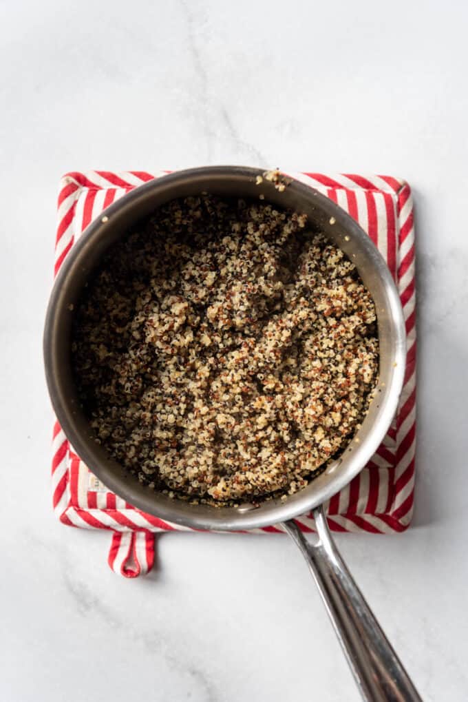 A pot of cooked quinoa on a striped hot pad.