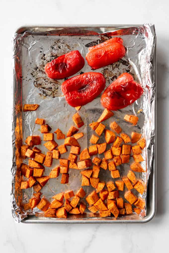 Roasted red bell peppers and bite-size chunks of sweet potato on a baking sheet lined with aluminum foil.