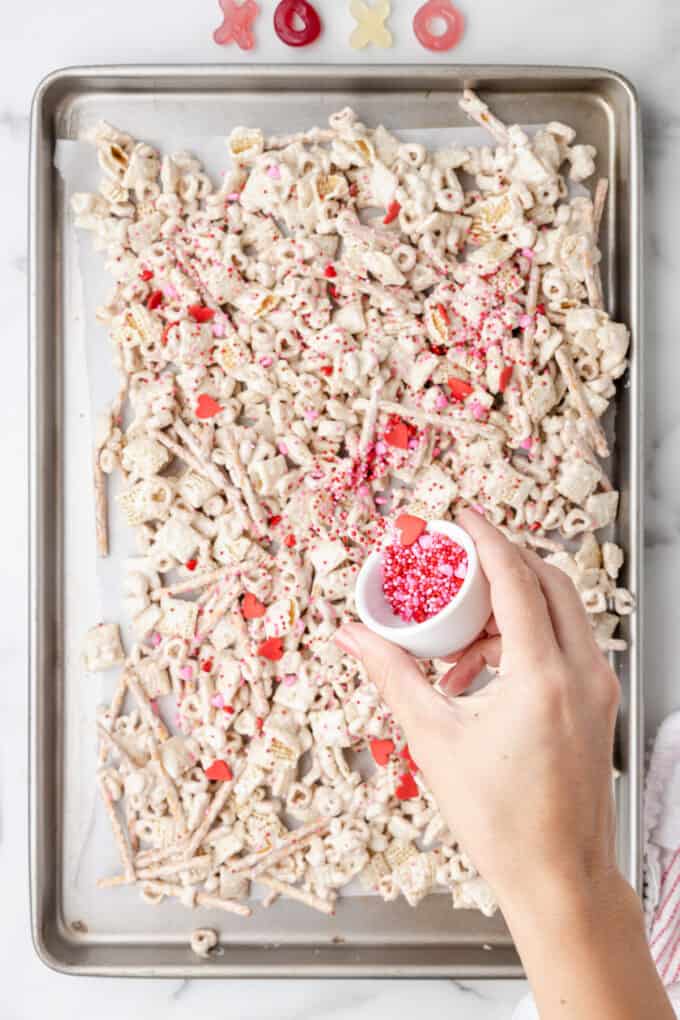 Adding sprinkles to white chocolate chex mix on a baking sheet.