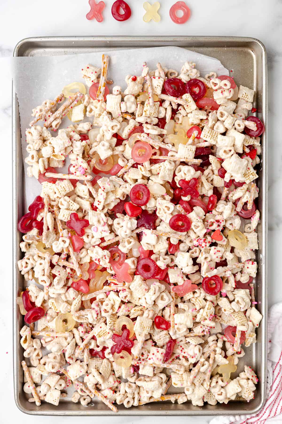 Mixing Valentine chex mix on a large baking sheet.