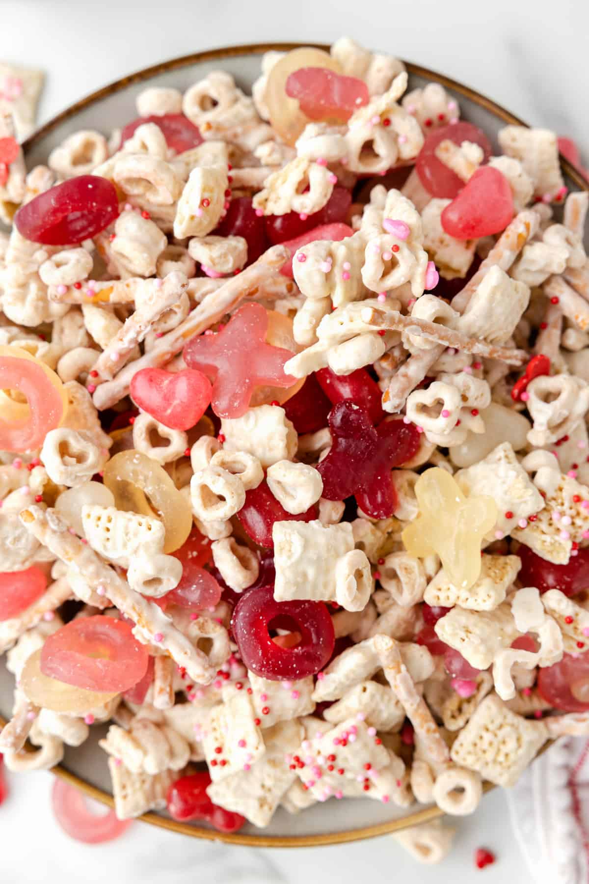 An overhead image of a bowl of Valentine snack mix with cheerios, chex cereal, pretzels, and more.