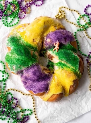 An overhead image of a king cake surrounded by Mardi Gras beads.