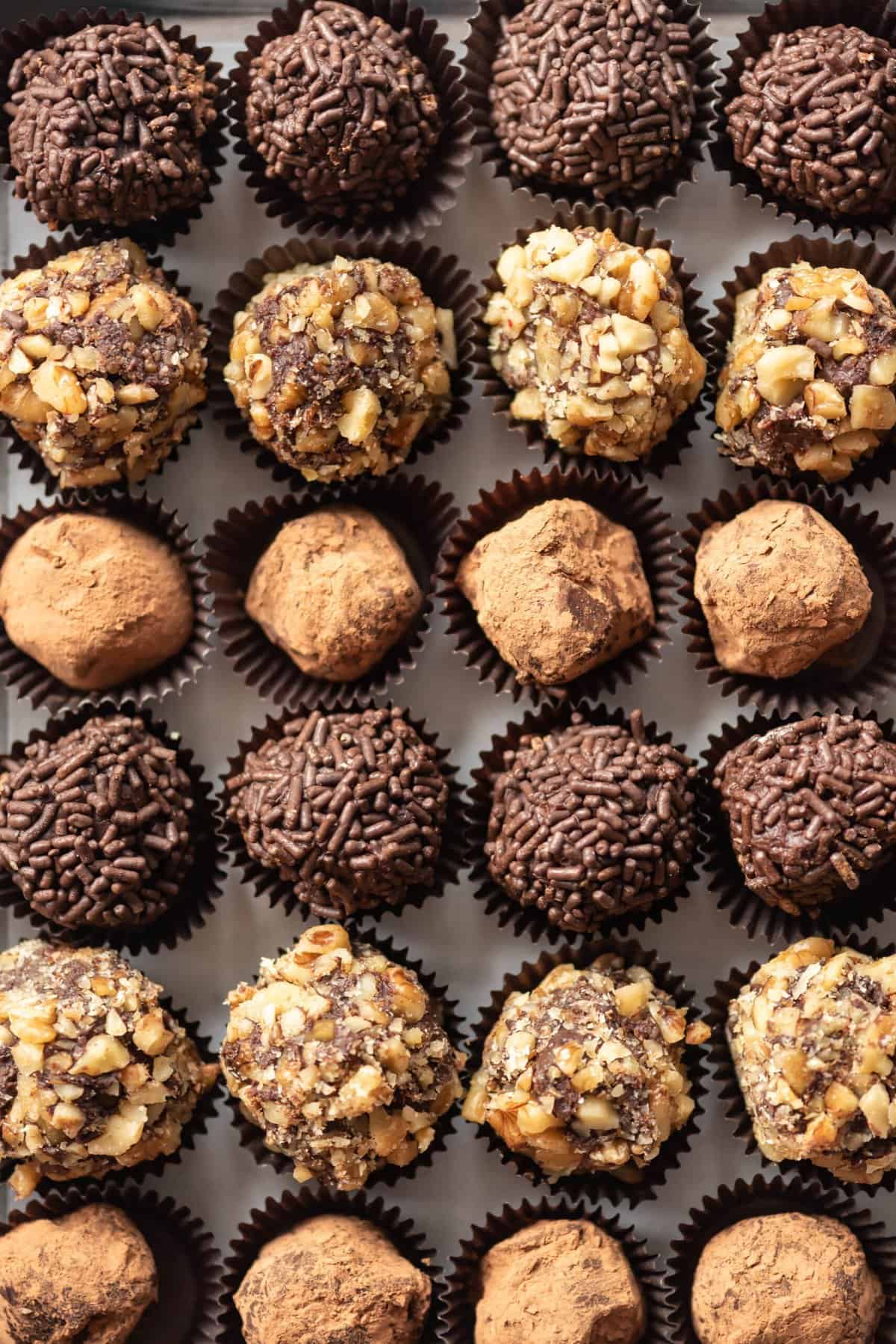 Rows of chocolate truffles coated in chopped walnuts, cocoa powder, and chocolate sprinkles.
