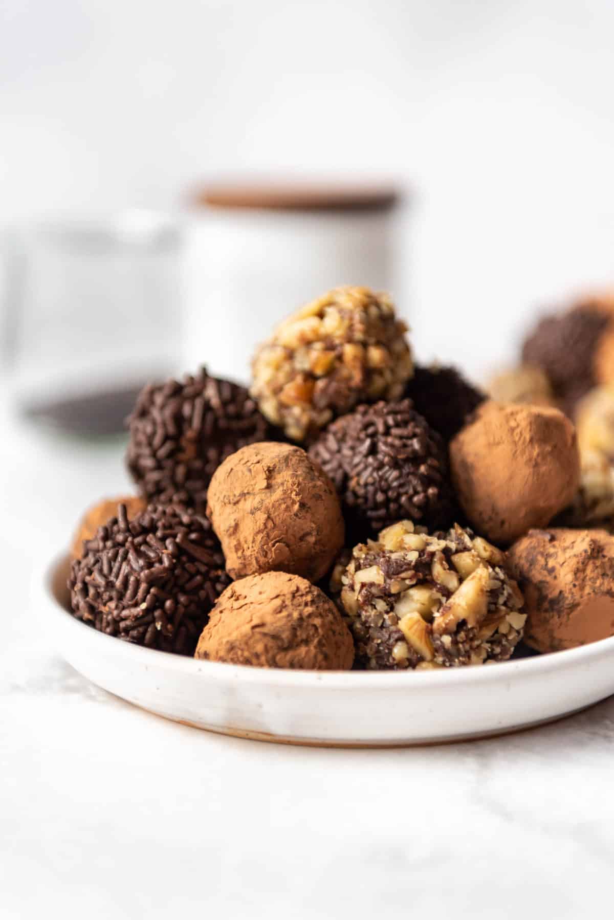 Homemade chocolate truffles coated in cocoa powder, sprinkles, and nuts on a white plate.
