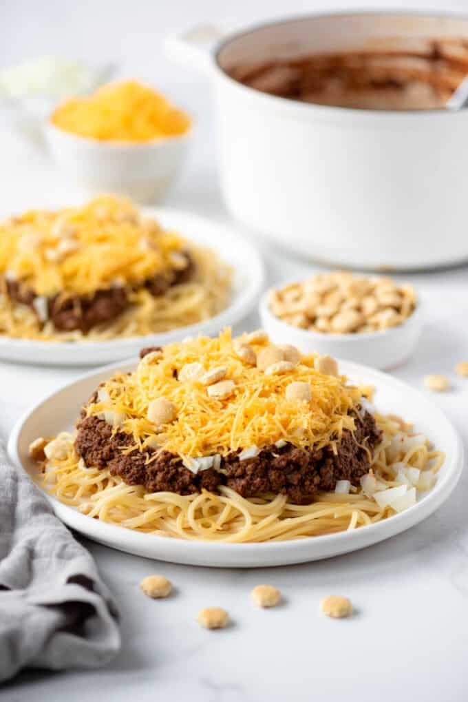 Two plates of Cincinnati chili in front of a white Dutch oven.