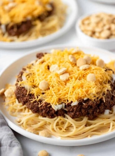A plate of copycat Skyline Cincinnati chili with pasta, oyster crackers, grated cheese, and chopped onions.