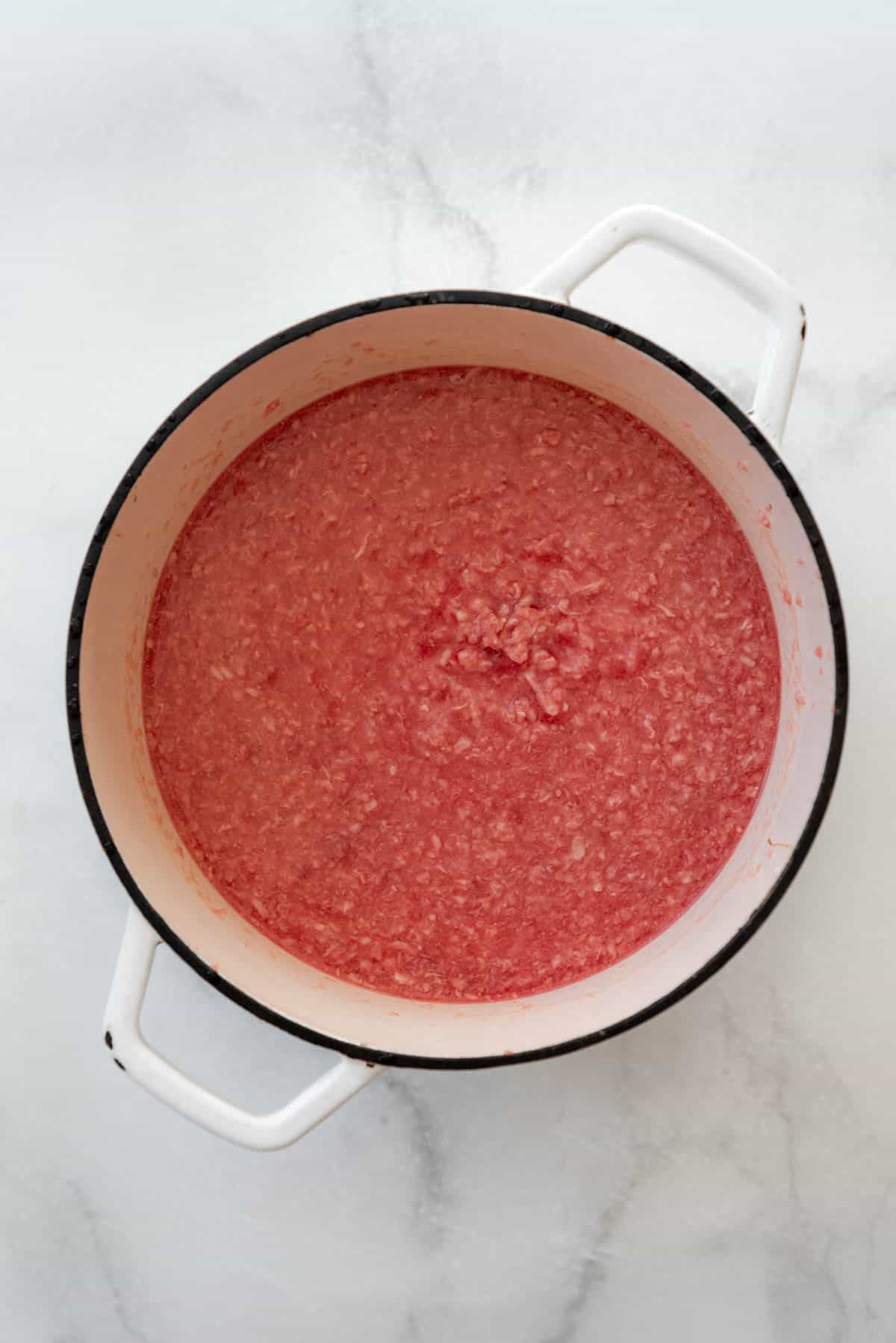 A large white Dutch oven filled with crumbled ground beef in water.