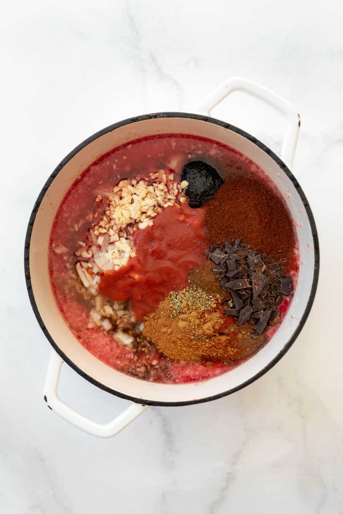 Adding spices, tomato sauce, garlic, and onions to a pot of water and ground beef.