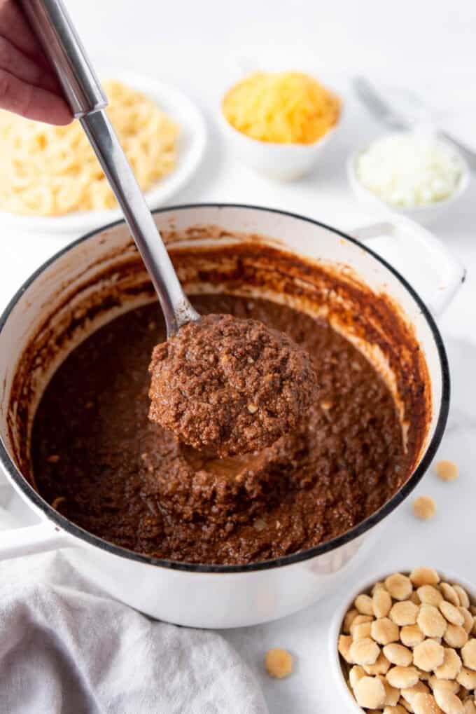 A ladle holding up a large spoonful of homemade Cincinnati chili over the pot of meat sauce.