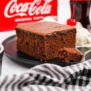 A slice of coca-cola cake on a black plate with a bite on a fork.