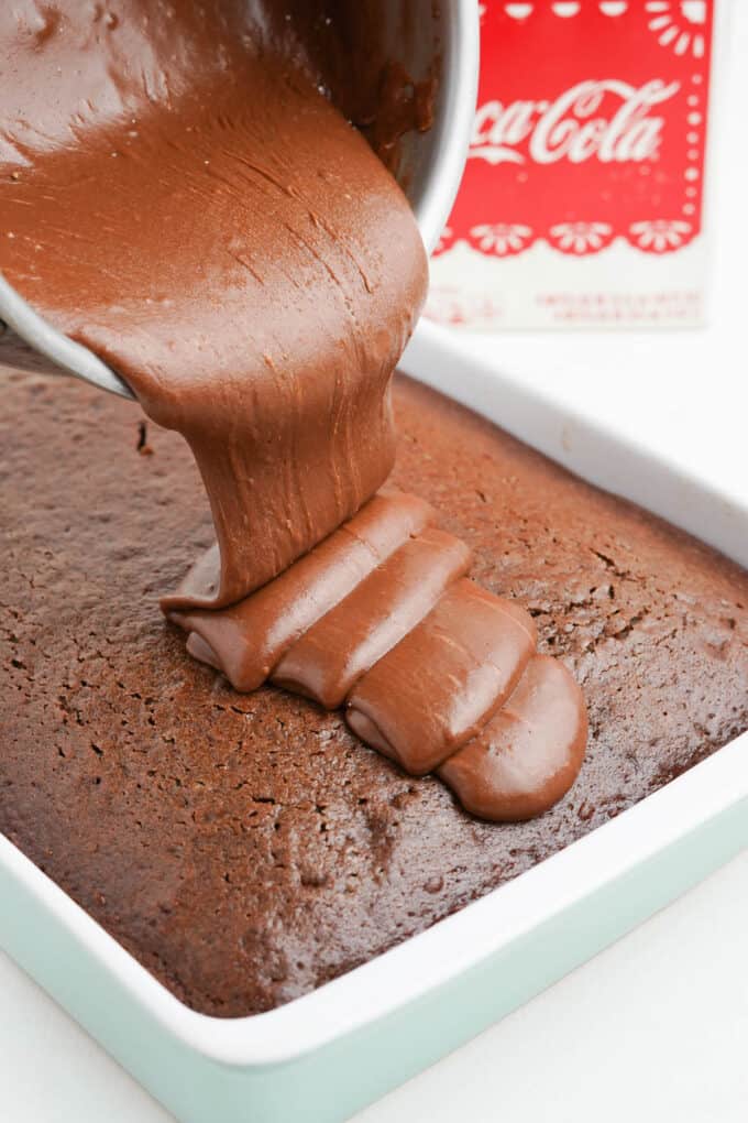 Pouring cooked chocolate coca cola frosting onto coca cola cake.