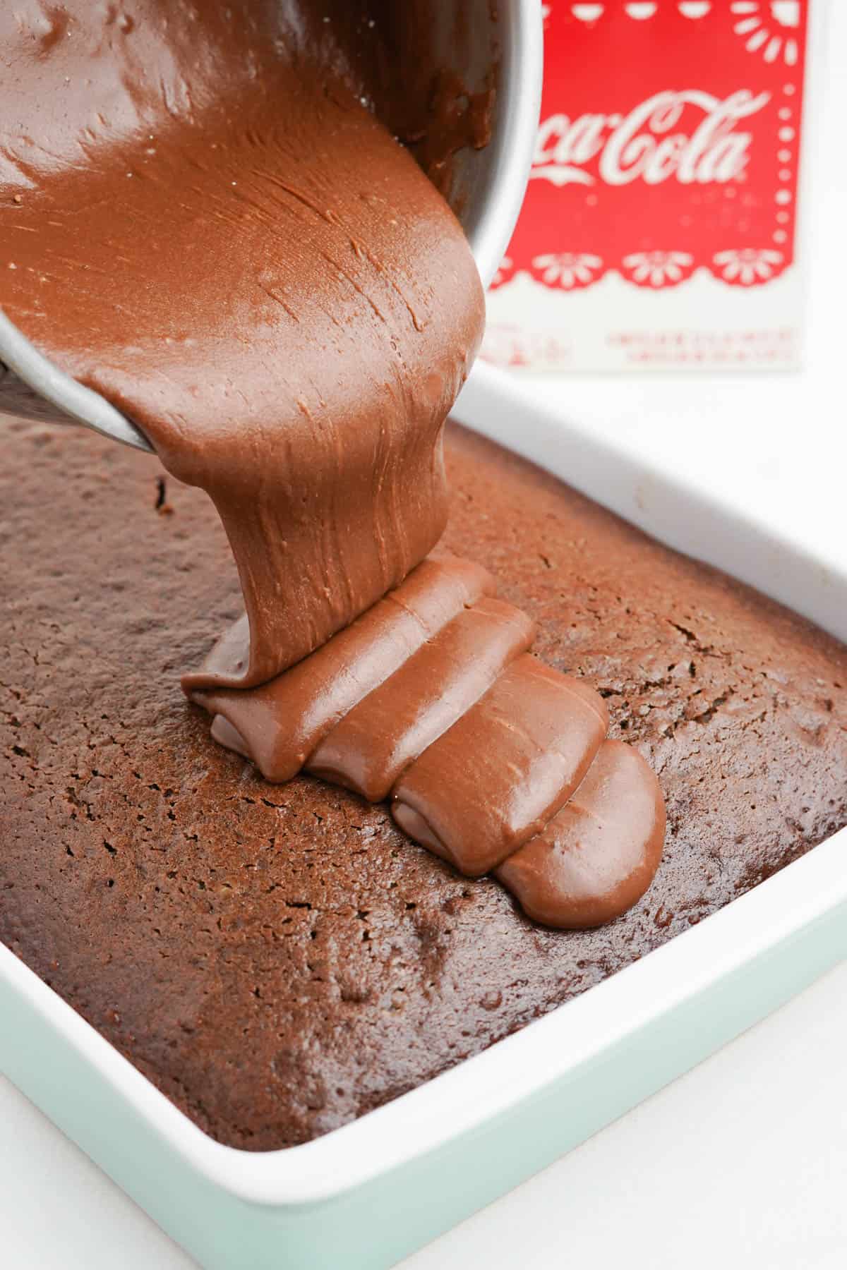 Pouring cooked chocolate coca cola frosting onto coca cola cake.