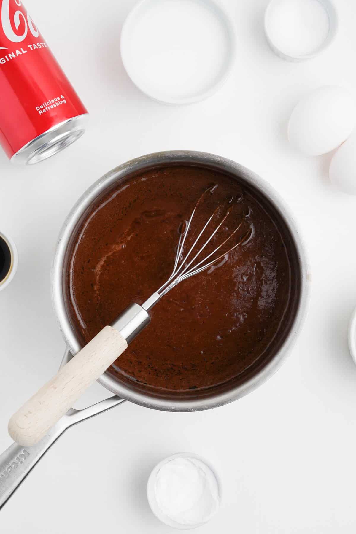 A whisk in cooked chocolate icing in a saucepan.