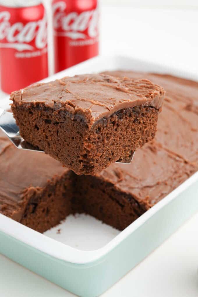 A spatula lifting a slice of coca-cola cake out of a baking dish.