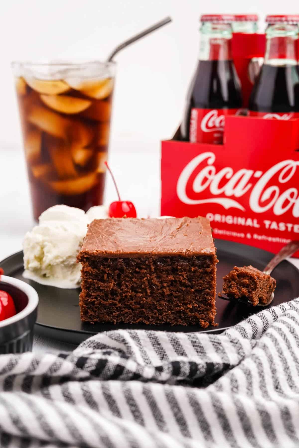 A piece of chocolate coca cola cake in front of a glass of coke and more bottles of soda.
