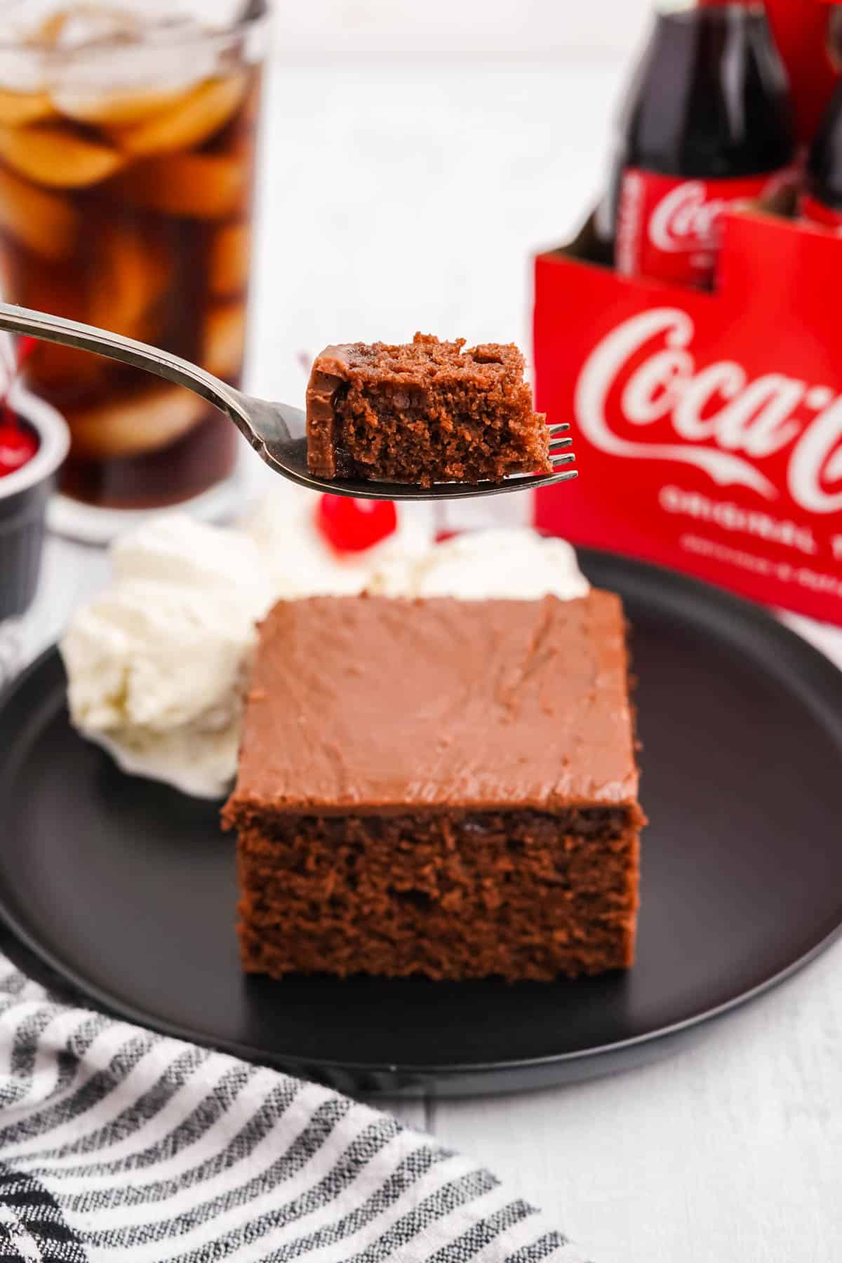 A fork lifting a bite of chocolate coca cola cake in front of a piece of cake.