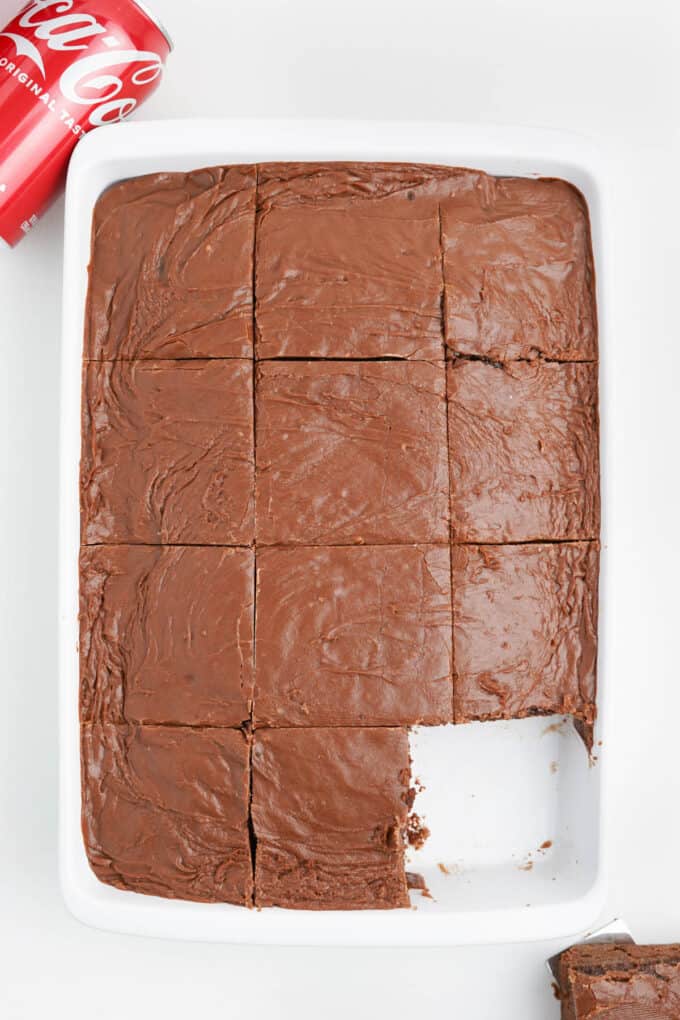 A frosted coca cola cake with one square cut out of it.