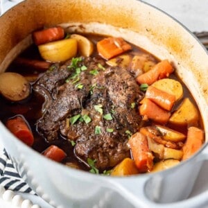 A large Dutch oven with pot roast, potatoes, and carrots.