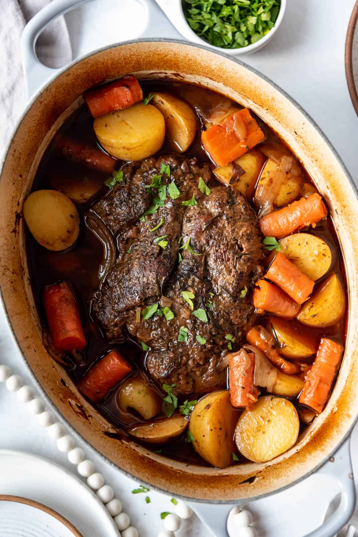 Parsley sprinkled over pot roast and vegetables in a Dutch oven.