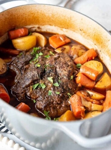A large Dutch oven with pot roast, potatoes, and carrots.
