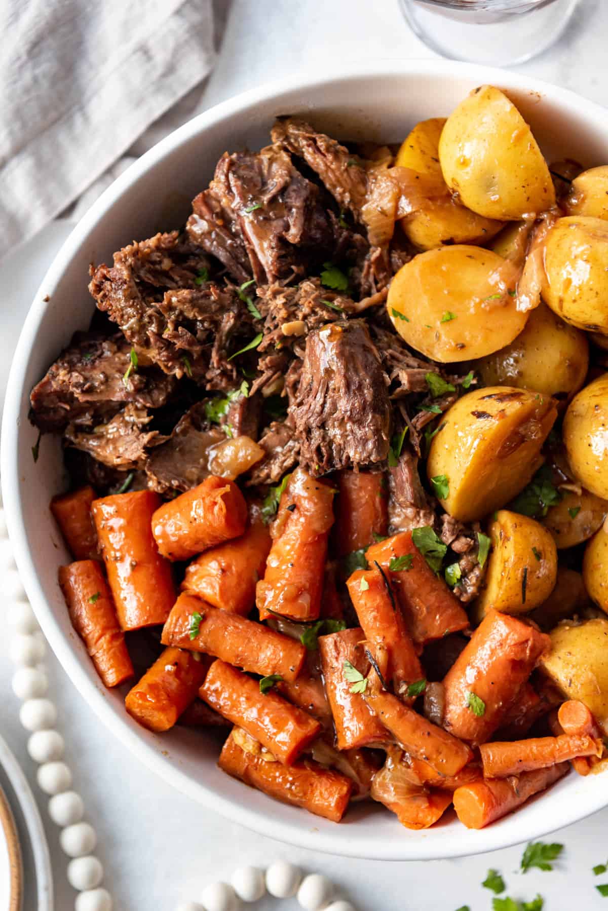 An overhead image of large chunks of roasted carrots, pot roast, and Yukon gold potatoes in a white serving bowl.