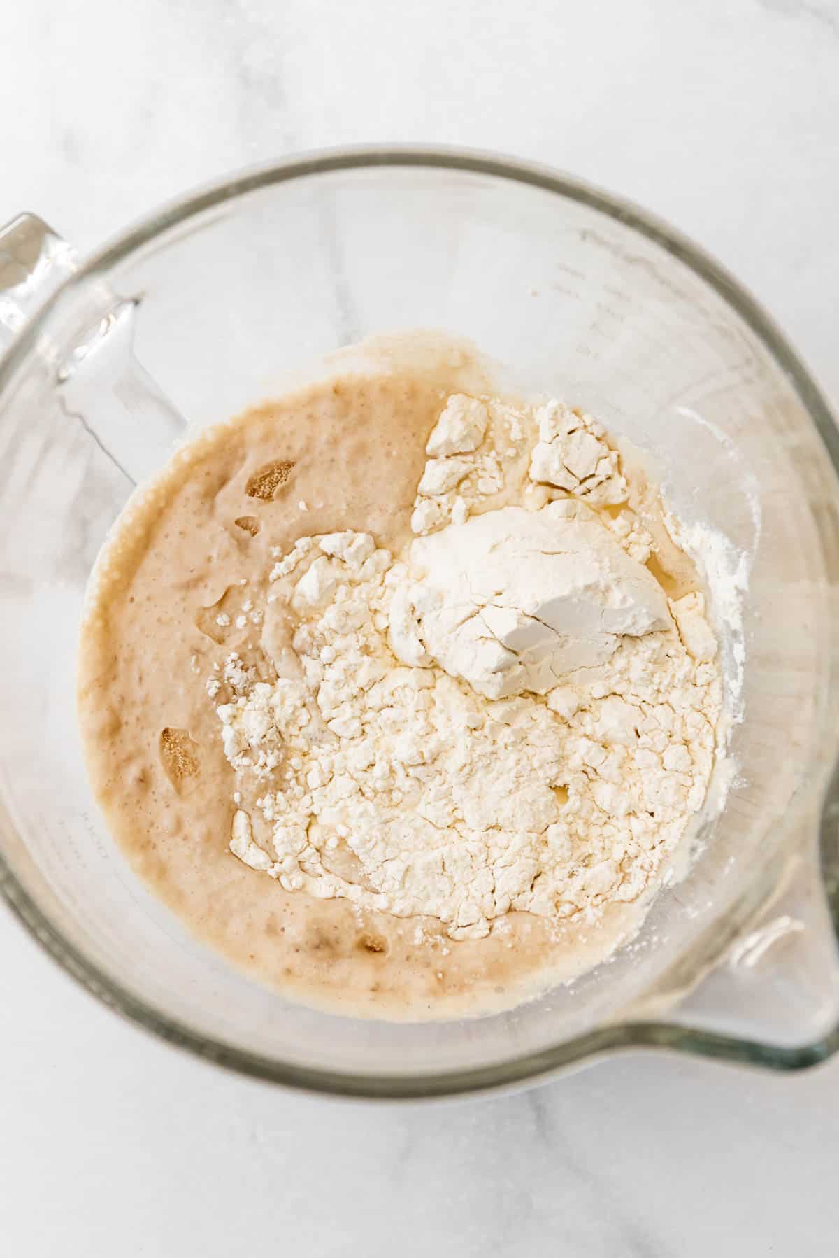 Adding flour and ingredients to proofed yeast in a glass bowl.