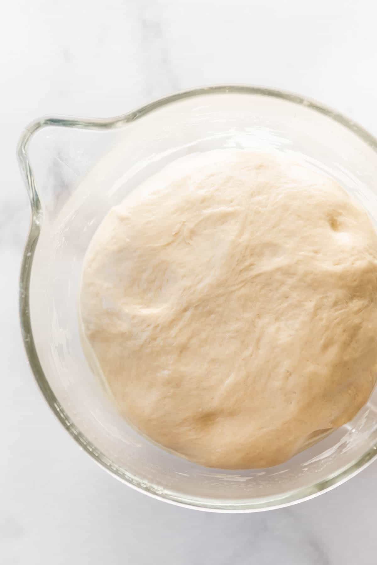 Risen bread dough in a glass bowl.