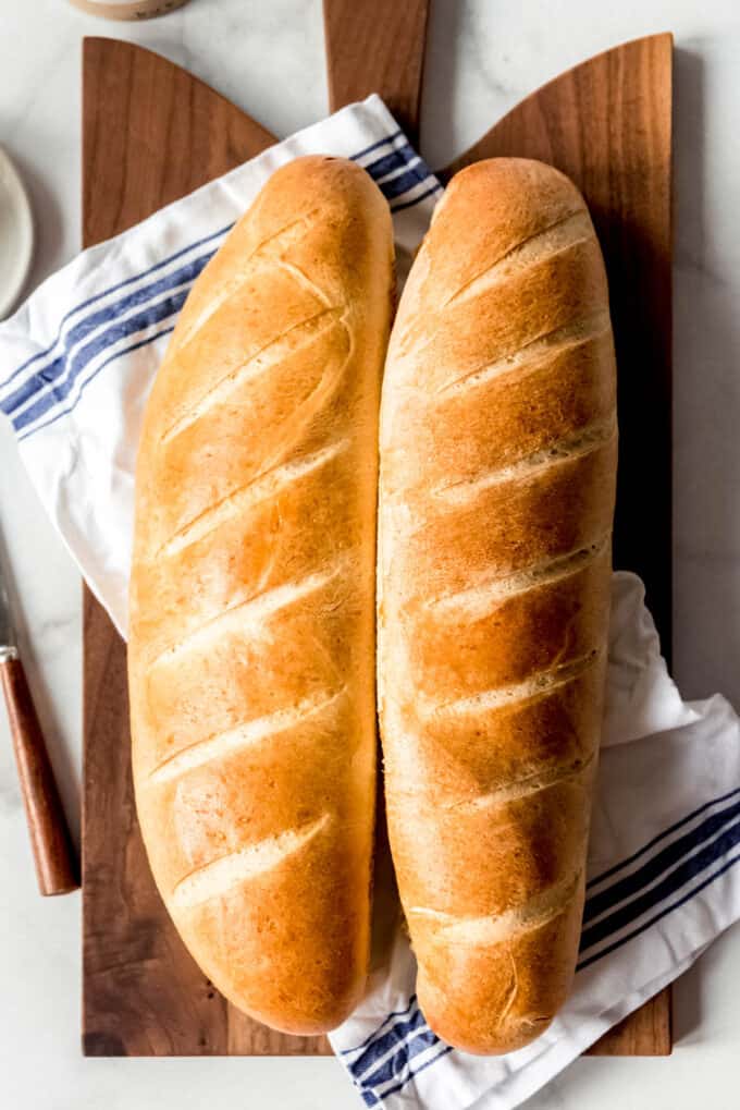 Two loaves of golden brown French bread on a cloth napkin on a cutting board.