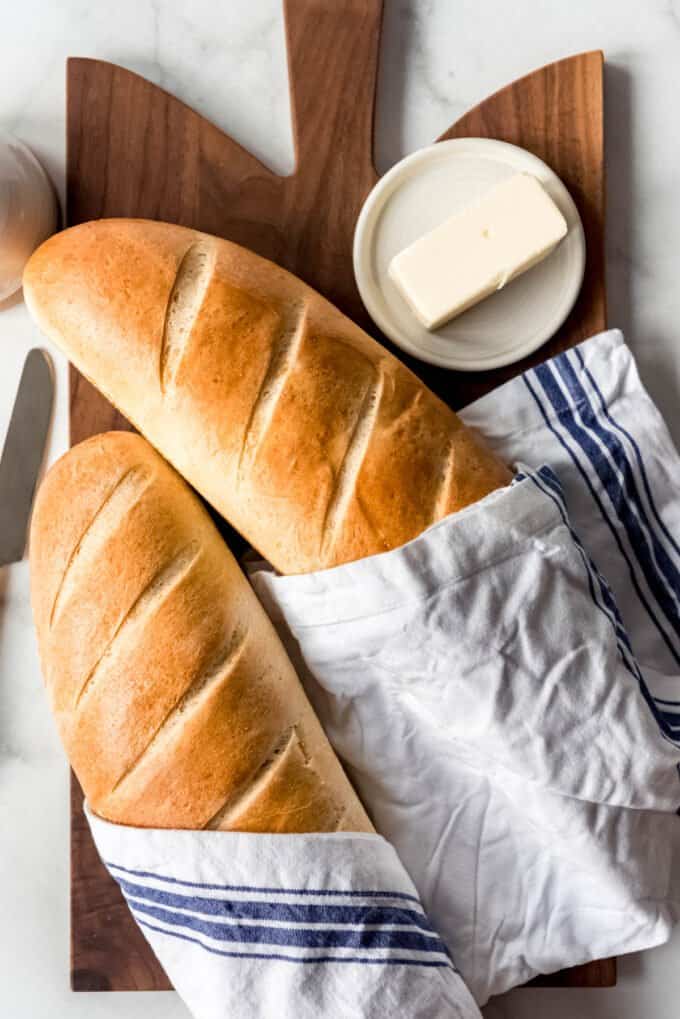 Two loaves of French bread wrapped in a cloth next to butter on a butter dish..